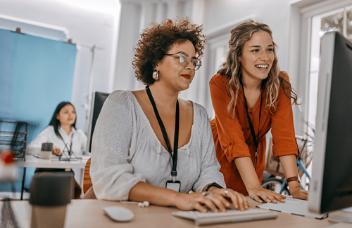 Two professionals collaborate at a computer in a bright office.