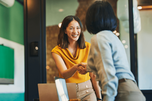 Two professionals smile and shake hands during a meeting.