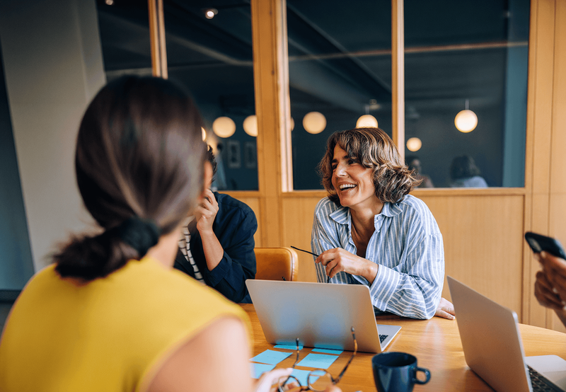 Three professionals collaborate around a table with a laptop during a casual meeting.